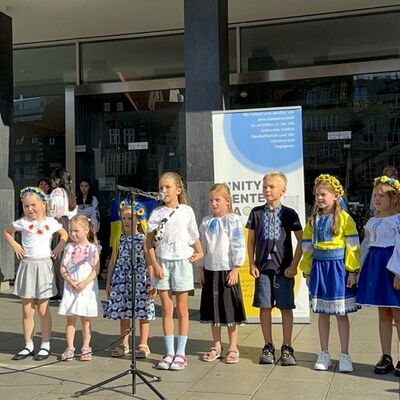 Mädchen und Jungen, zum Teil in gelb-blauen Trachten stehen mit einem Mikro vor der Bürgerschaft