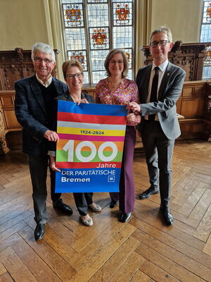 4 Personen halten ein Plakat mit der Aufschrift 100 Jahre Der Paritätische Bremen