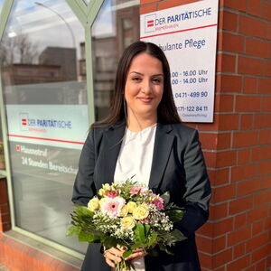 Eine junge Frau mit Blumenstrauß, im Hintergrund ein Schild des Paritätischen BHV, Ambulante Pflege