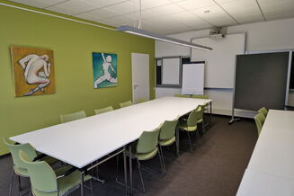 Seminarraum mit großem Tisch, grünen Stühlen, im Hintergrund, Whiteboard, Flipchart