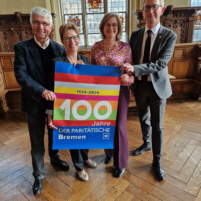 4 Personen halten ein Plakat mit der Aufschrift 100 Jahre Der Paritätische Bremen