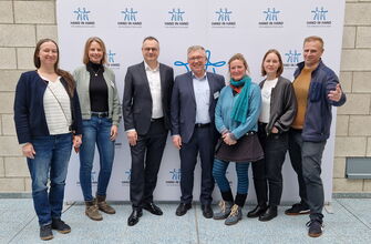7 Personen vor einer Logowand Hand in Hand für Norddeutschland