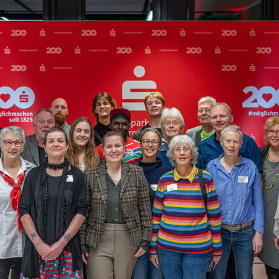 Gruppe von freudigen Menschen vor einer roten Wand der Sparkasse