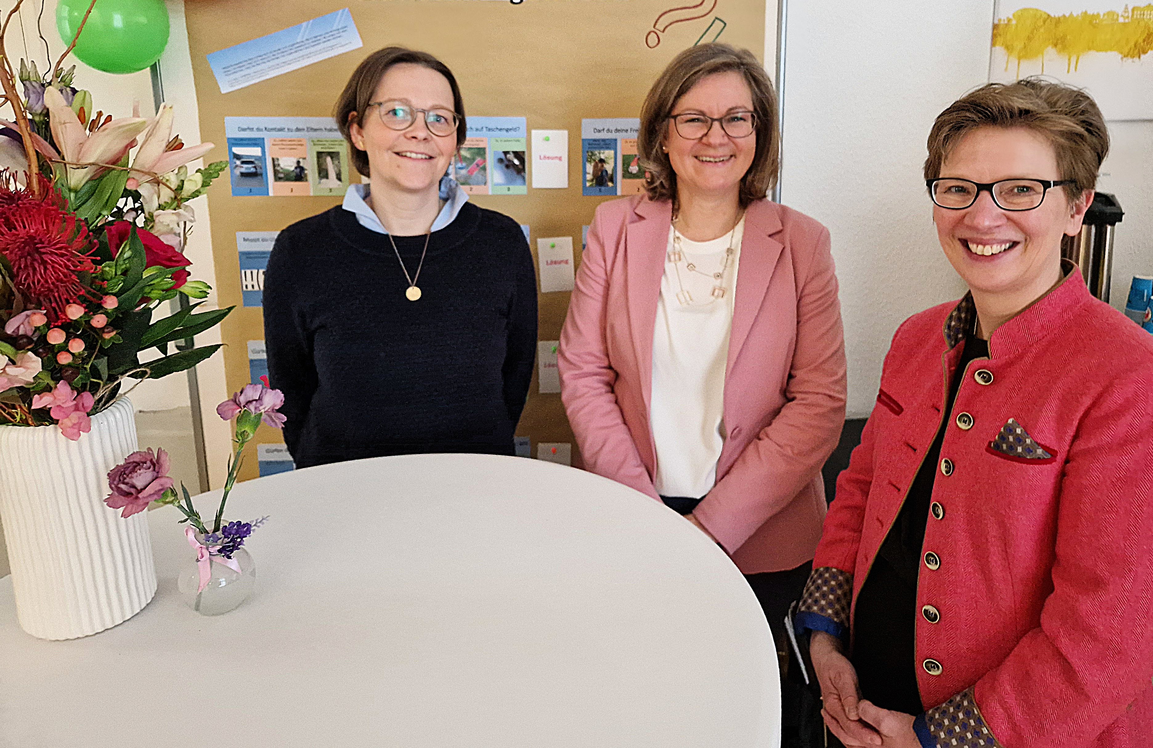 3 Frauen lächelnd an einem Stehtisch mit Blumen